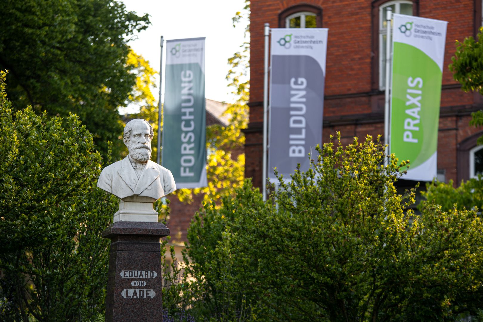 Campus der Hochschule Geisenheim University mit Fahnen „Forschung“, „Bildung“ und „Praxis“