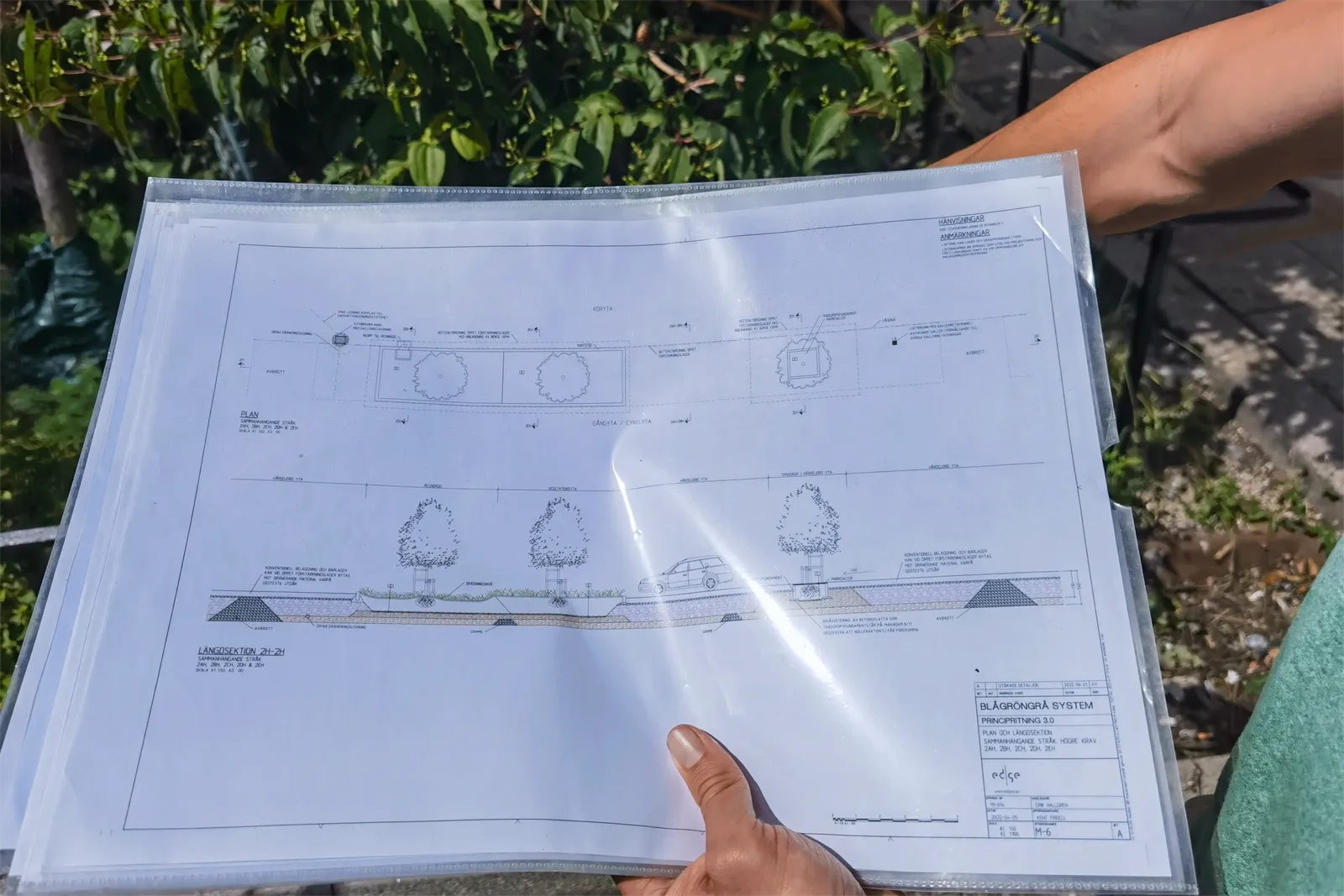 Hände halten einen laminierten Plan mit einem Querschnitt des Straßenaufbaus