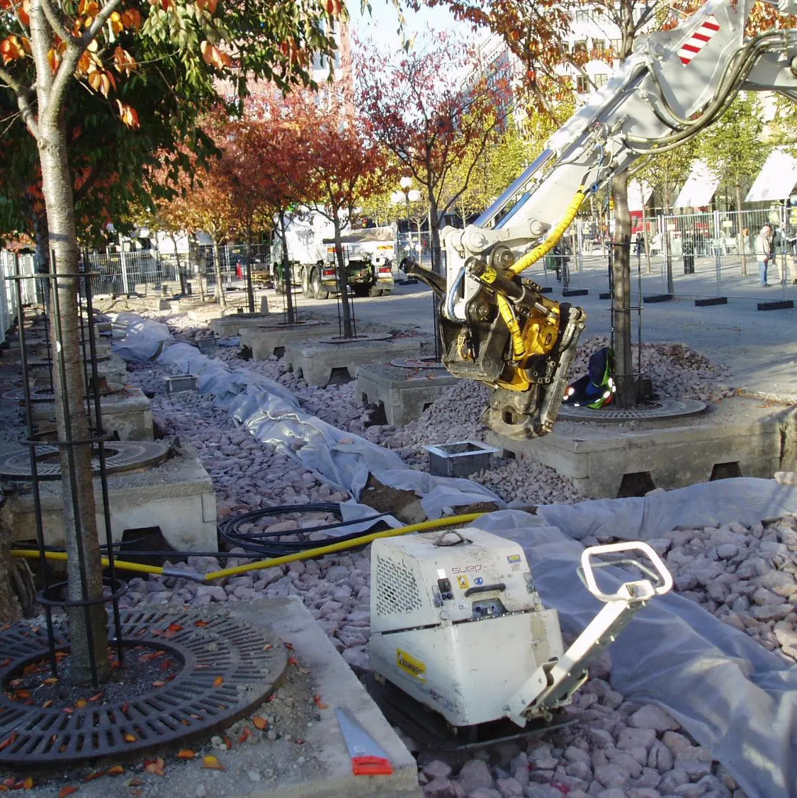 Baustelle mit eingebautem grobem Schotter, Bäumen in Einfassungen und einer Rüttelplatte