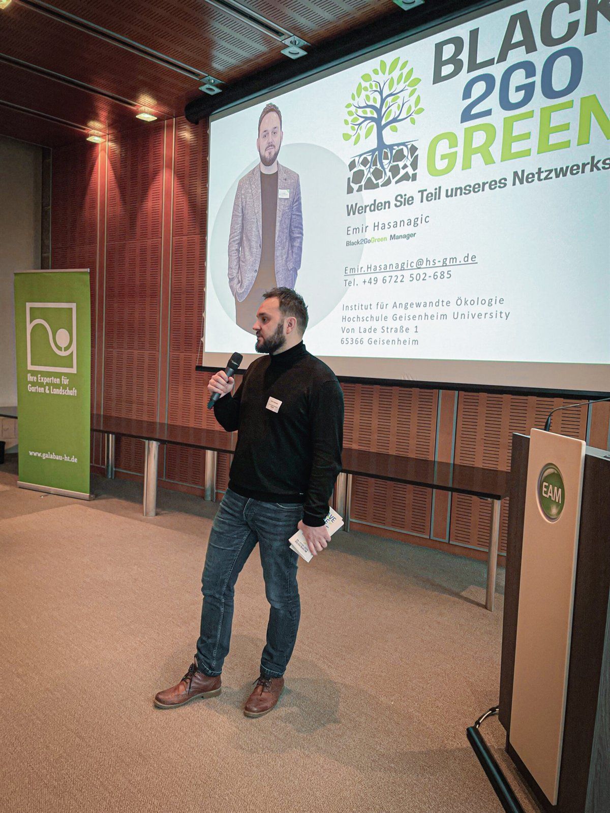 Emir Hasanagić hält einen Vortrag vor einer Leinwand mit dem Black2GoGreen-Logo