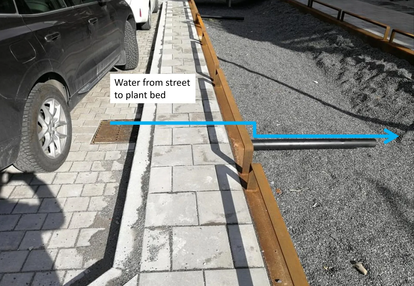 Pflasterrinne mit Pfeil und der Beschriftung „Water from street to plant bed“